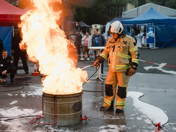 Nacht der Technik Köln Ein Feuerwehrmann in vollständiger Ausrüstung steht neben einem brennenden Metallfass.