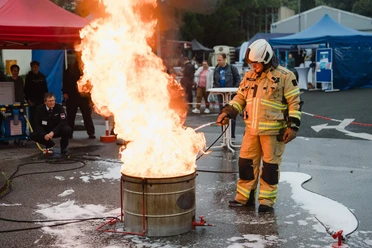 Night of Technology Cologne A firefighter in full equipment stands next to a burning metal barrel.