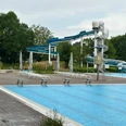 Freizeitbad Münchehagen: Großer Außenbereich mit Wasserrutsche, umgeben von Bäumen und Liegestühlen.Münchehagen leisure pool: Large outdoor area with water slide, surrounded by trees and sun loungers.Münchehagen fritidspool: Stort udendørs område med vandrutsjebane, omgivet af træer og liggestole.Vrijetijdszwembad Münchehagen: Groot buitengedeelte met waterglijbaan, omgeven door bomen en ligstoelen.