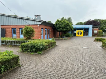 Freizeitbad Münchehagen Schwimmbad mit blau-rotem Gebäude und gelber Eingangstür, umgeben von grünen Büschen und Bäumen.Swimming pool with blue and red building and yellow entrance door, surrounded by green bushes and trees.Swimmingpool med blå og rød bygning og gul indgangsdør, omgivet af grønne buske og træer.Zwembad met blauw en rood gebouw en gele toegangsdeur, omringd door groene struiken en bomen.