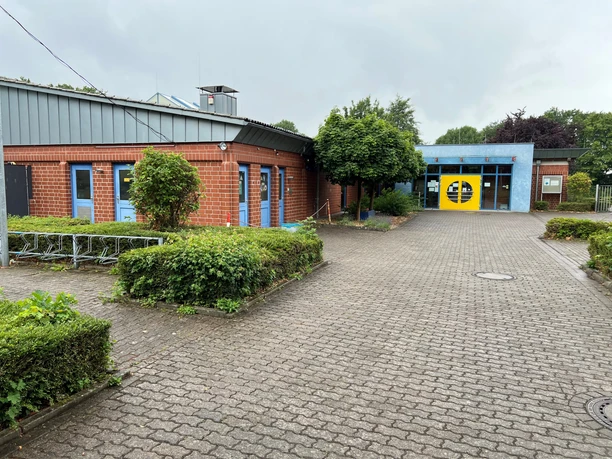 Freizeitbad Münchehagen Swimming pool with blue and red building and yellow entrance door, surrounded by green bushes and trees.