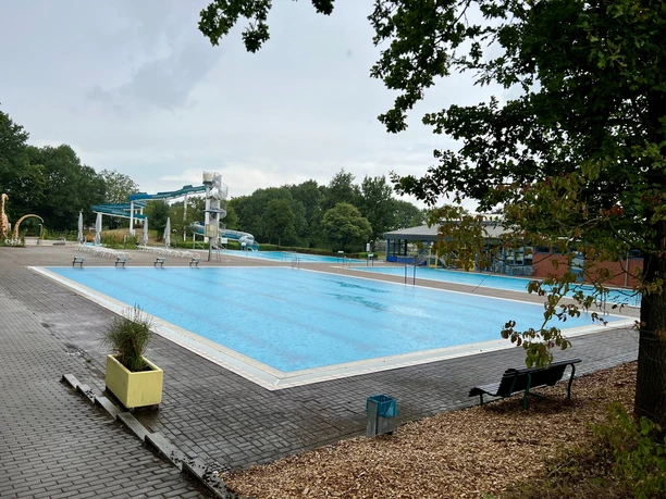 Freizeitbad Münchehagen A large outdoor pool with turquoise blue water, surrounded by trees and equipped with slides.