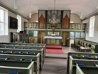 Friedhofskapelle Winzlar Die Friedhofskapelle Winzlar ist innen schlicht gestaltet mit grünen Holzbänken und einem Altar.
