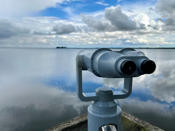 Teleskop am Winzlarer Turm mit weitem Blick auf den wolkigen, spiegelnden See an einem klaren Tag.