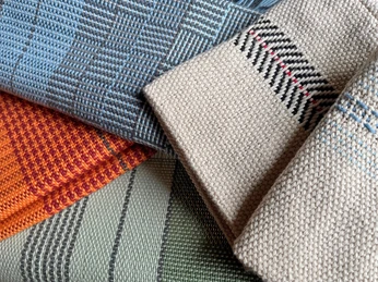 Muster weben Titel.jpg Detailaufnahme handgewebter Stoffmuster in verschiedenen Farben und Webtechniken. Zu sehen sind komplexe Muster in Blau, Orange, Grün und Beige mit feinen Details.Close-up of hand-woven fabric patterns in various colors and weaving techniques. You can see complex patterns in blue, orange, green and beige with fine details.Détail de motifs de tissus tissés à la main dans différentes couleurs et techniques de tissage. On y voit des motifs complexes en bleu, orange, vert et beige avec des détails fins.