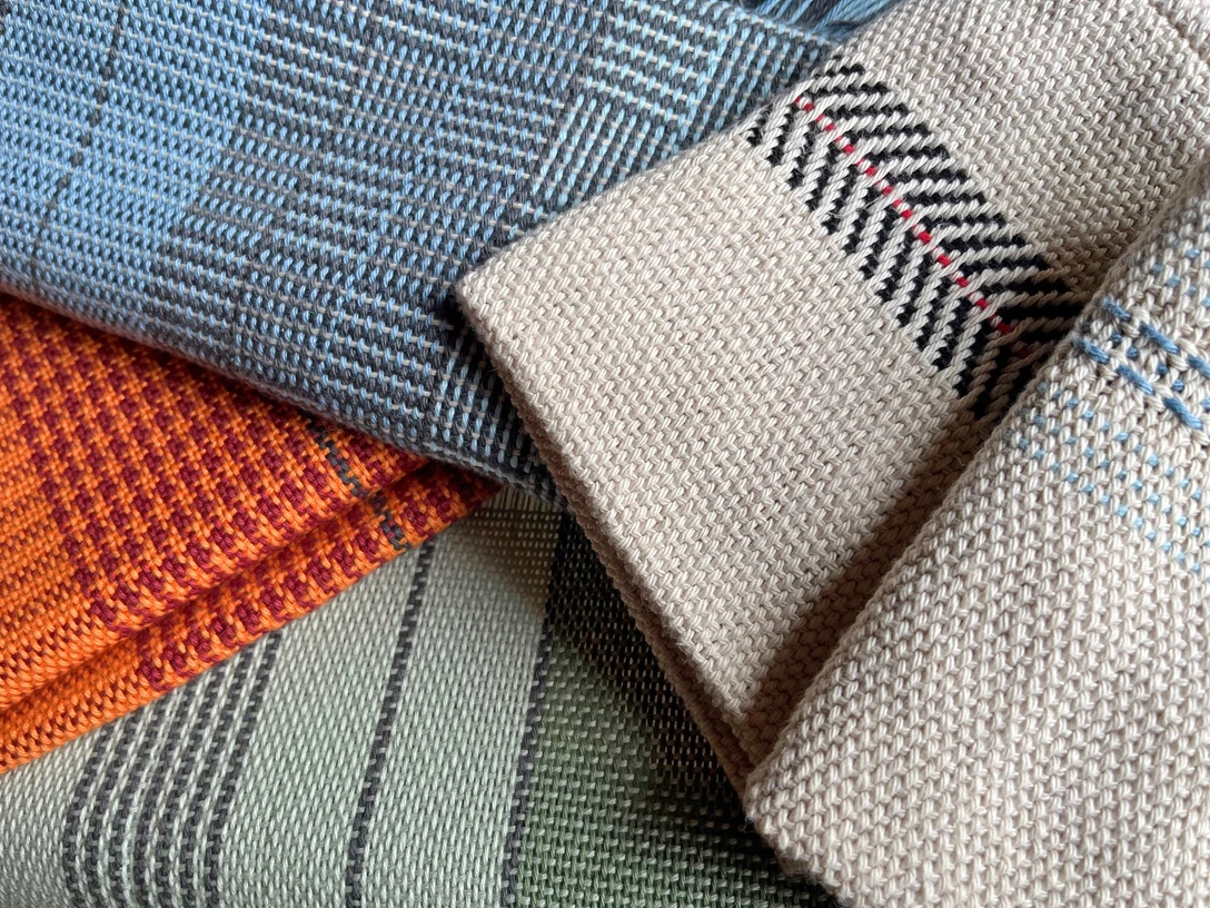 Pattern weave title.jpg Detailaufnahme handgewebter Stoffmuster in verschiedenen Farben und Webtechniken. Zu sehen sind komplexe Muster in Blau, Orange, Grün und Beige mit feinen Details.Close-up of hand-woven fabric patterns in various colors and weaving techniques. You can see complex patterns in blue, orange, green and beige with fine details.Détail de motifs de tissus tissés à la main dans différentes couleurs et techniques de tissage. On y voit des motifs complexes en bleu, orange, vert et beige avec des détails fins.
