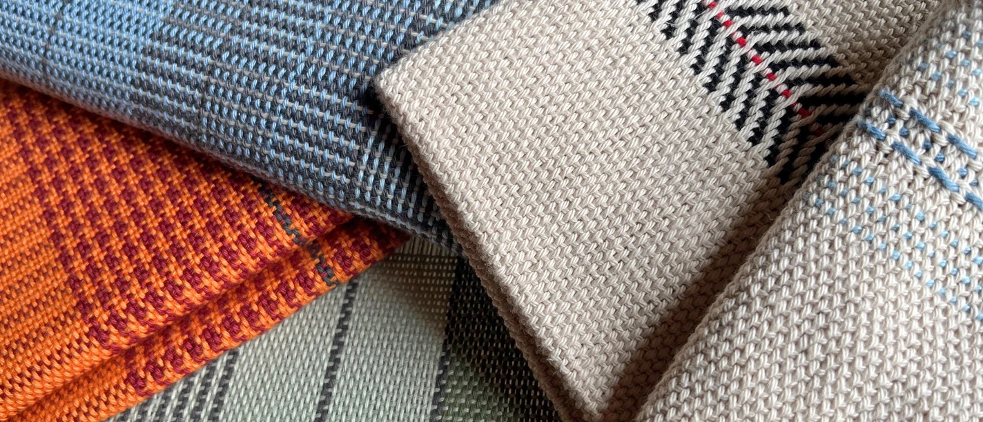 Tissage d'échantillons Titre.jpg Détail de motifs de tissus tissés à la main dans différentes couleurs et techniques de tissage. On y voit des motifs complexes en bleu, orange, vert et beige avec des détails fins.