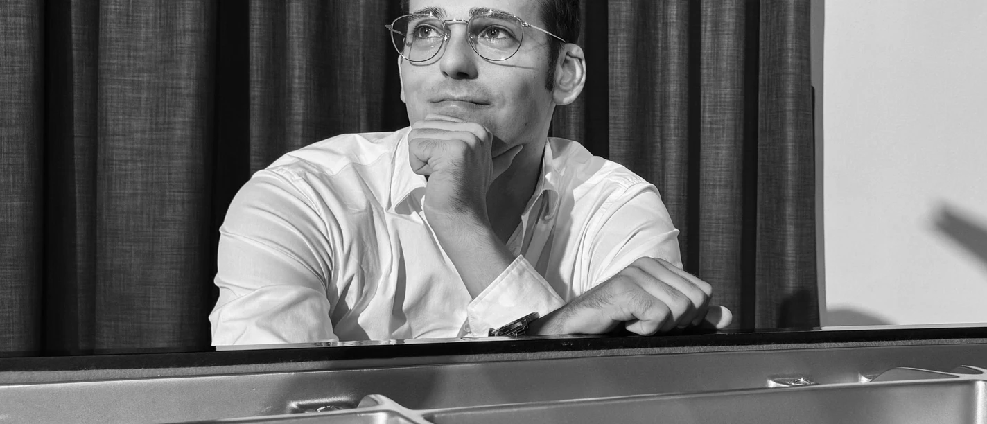 Jonas Becker.jpg Ein Mann sitzt nachdenklich am Klavier