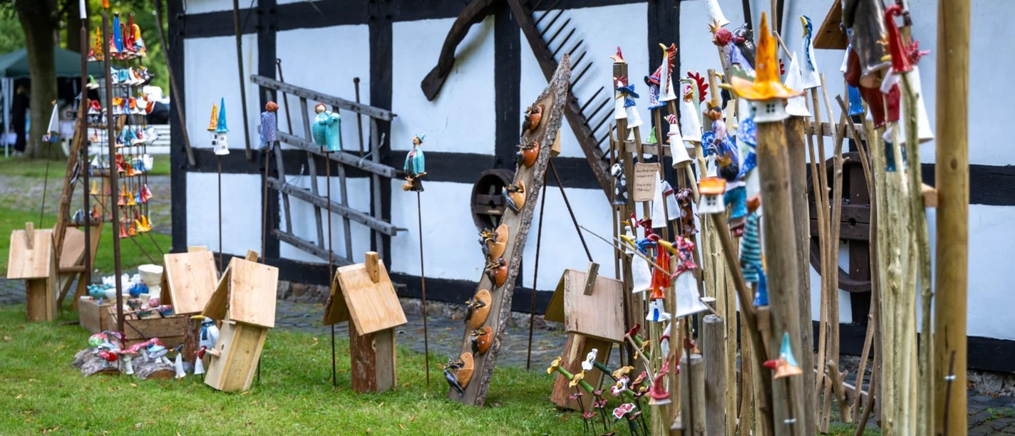 Kunst_Handwerkermarkt 2024.jpg Bunte Kunsthandwerke aus Holz und Keramik vor historischem Fachwerkhaus in Aschen
