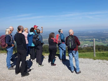 Aktivwoche-Wanderung-Berge.jpg Eine Wandergruppe genießt den Ausblick auf grüne Hügel und weite Landschaft unter klarem Himmel.