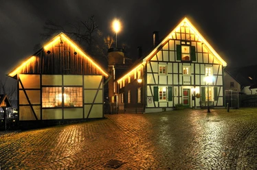 Fachwerkhäuser bei Nacht mit warm erleuchteten Fenstern und Kopfsteinpflaster im Vordergrund.