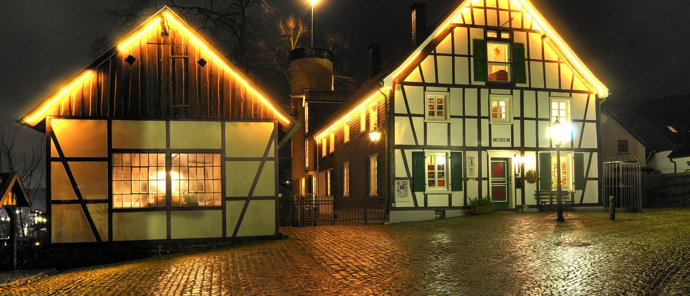 Fachwerkhäuser bei Nacht mit warm erleuchteten Fenstern und Kopfsteinpflaster im Vordergrund.