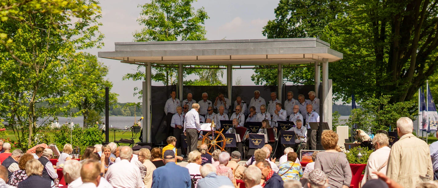 shanty-festival-kurpark-buehne Shanty Chor auf der Freilichtbühne am Zwischenahner Meer, im Vordergrund interessierte, ältere Zuhörer