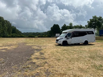 Ein Wohnmobil steht auf einem weitläufigen, grasbewachsenen Stellplatz unter einem bewölkten Himmel.
