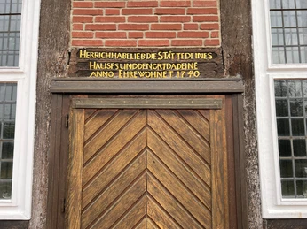 Eingangstür der historischen Friedhofskapelle Winzlar mit hölzernem Zickzack-Muster und Inschrift.