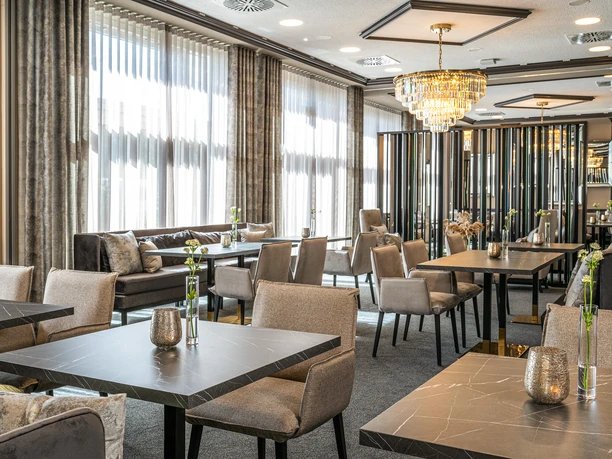 Victor’s Residenz-Hotel Gummersbach Elegantes Restaurant mit modernen Tischen, grauen Stühlen und einem Kronleuchter an der Decke.