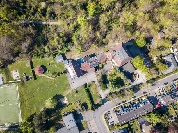 Das Gelände der Jugendherberge Velbert von oben Luftaufnahme der Jugendherberge Velbert, umgeben von viel Grün, nahe einem Sportplatz und einer Straße.