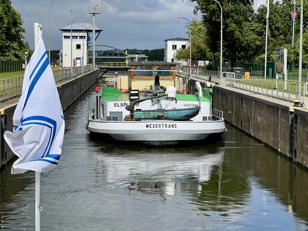 A cargo ship named Wesertrans passes through the Langwedel lock, surrounded by green nature.