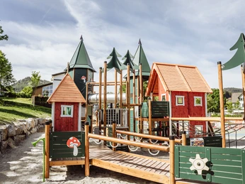 Buntes Klettergerüst mit Bäumen und roten Häuschen auf dem Inklusionsspielplatz Baiersbronn