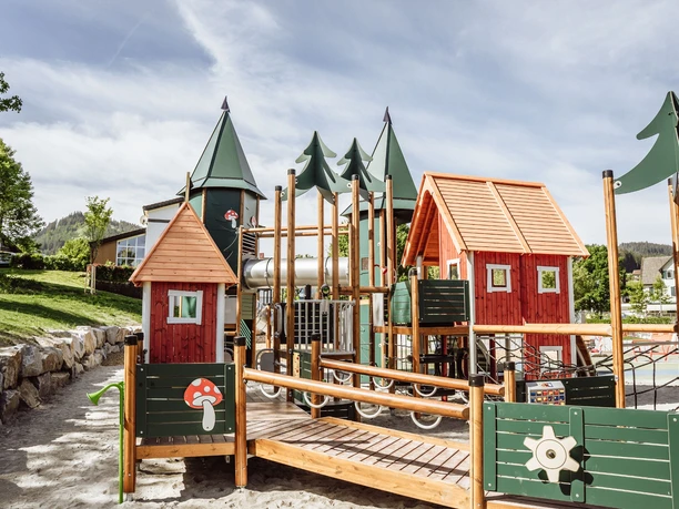 Buntes Klettergerüst mit Bäumen und roten Häuschen auf dem Inklusionsspielplatz Baiersbronn