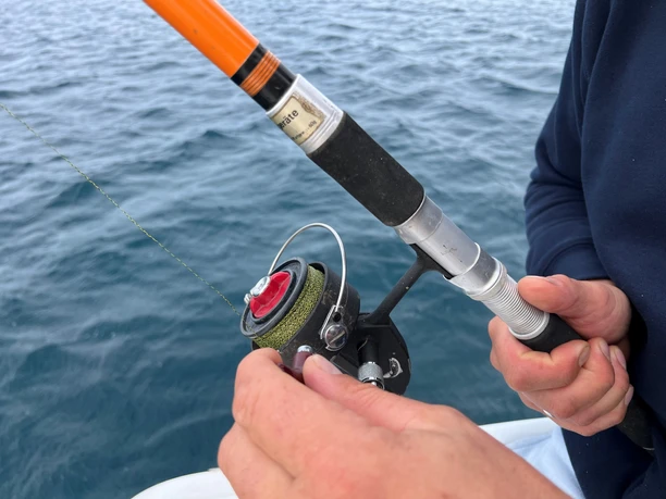 Mann mit Angel Ein Mann hält eine Angelrute über ruhigem Gewässer. Hände fokussiert, bereit zum Fischen.