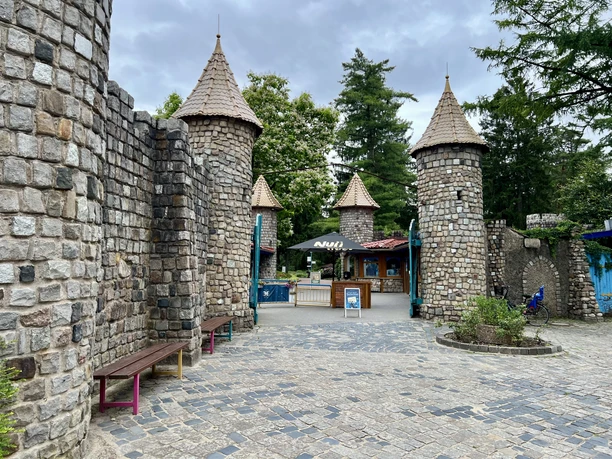 Magic Park Verden Entrance to a leisure park with stone towers and cobblestones, surrounded by green trees.