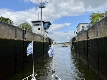 Schleuse Langwedel Schleuse in Betrieb mit geöffneten Toren, dahinter Wasserweg durch grüne Landschaft, bedeckter Himmel.