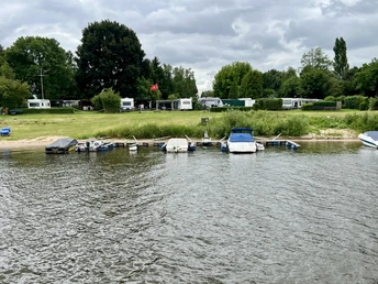 Campingplatz Horstedt mit Wohnwagen und Zelten am Flussufer, umgeben von saftigem Grün.