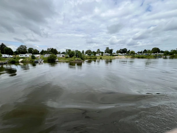 Weitläufiger Campingplatz am ruhigen Fluss beherbergt Wohnmobile und Zelte unter bedecktem Himmel.
