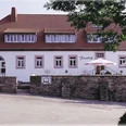 Außenansicht des Hotels, weißes Gebäude, im vorderen Bereich Terrasse mit Sonnenschirmen, umgeben von einer Mauer
