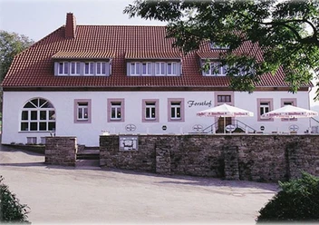 Hotel-Restaurant Forsthof Außenansicht des Hotels, weißes Gebäude, im vorderen Bereich Terrasse mit Sonnenschirmen, umgeben von einer Mauer