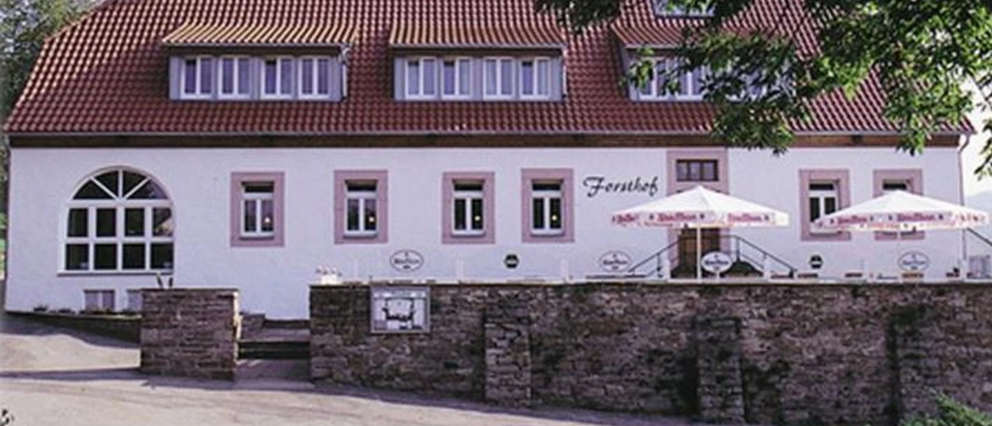 Hotel-Restaurant Forsthof Außenansicht des Hotels, weißes Gebäude, im vorderen Bereich Terrasse mit Sonnenschirmen, umgeben von einer Mauer