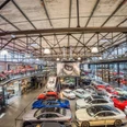 MS Hangar Ein großer, modernen Hangars mit einer beeindruckenden Sammlung von Fahrzeugen. Verschiedene Sportwagen in leuchtenden Farben, wie Rot, Blau und Weiß, sind auf dem Hallenboden ausgestellt. Oben links gibt es eine Galerieebene mit weiteren Exponaten. Die Dachkonstruktion ist aus Stahl und verleiht dem Raum einen industriellen Charme. Licht geht von mehreren Leuchten ab und sorgt für eine helle, einladende Atmosphäre.A large, modern hangar with an impressive collection of vehicles. Various sports cars in bright colors, such as red, blue and white, are displayed on the hangar floor. Above left there is a gallery level with further exhibits. The roof construction is made of steel and gives the room an industrial charm. Light emanates from several luminaires and creates a bright, inviting atmosphere.