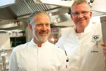 Brüder Wilbrand Zwei lächelnde Köche in weißer Kochkleidung stehen in einer professionellen Restaurantküche.