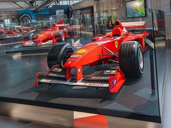 Ferrari Formula 1 racing car Ein roter Ferrari-Rennwagen in einem Museum, umgeben von Glaswänden, ausgestellt vor einer großen Fensterfront.A red Ferrari racing car in a museum, surrounded by glass walls, displayed in front of a large window front.