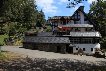 Außenansicht Traditionelles Fachwerkhaus inmitten grüner Natur mit blühendem Garten und blauen Himmel im Hintergrund.