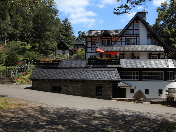 Außenansicht Traditionelles Fachwerkhaus inmitten grüner Natur mit blühendem Garten und blauen Himmel im Hintergrund.