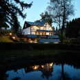 Außenansicht in der Dämmerung Ein idyllisches Haus am Waldrand beleuchtet die Abenddämmerung, spiegelt sich im ruhigen Teich.