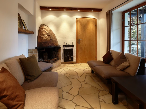 Gemütliches Wohnzimmer mit zwei Sofas, Kamin mit Holztüren und Steinboden; warmes, einladendes Ambiente.