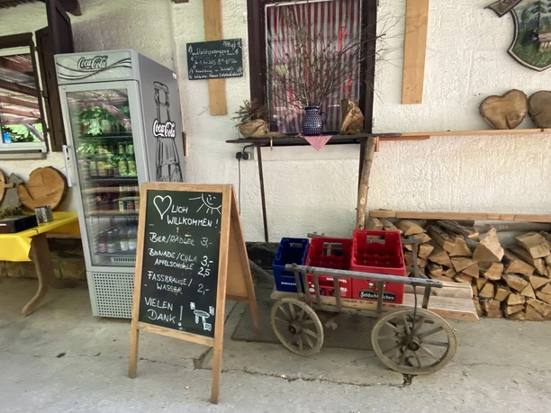 Drinks fridge and price board next to old wooden decorations and wooden trolleys with empty drinks crates.