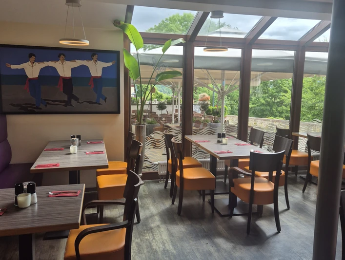 1000086999.jpg Ein helles, modernes Restaurant mit Panoramafenstern, buntem Interieur und üppigem Außenblick.