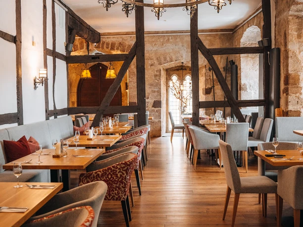 Bild_-2.jpg Ein rustikales Restaurant mit Holzbalken, stilvoll eingedeckten Tischen und einem auffälligen Kronleuchter.