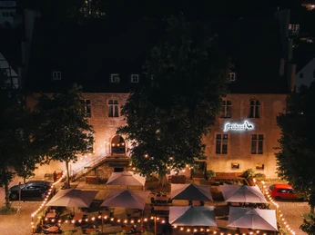 IMG_3178.JPG Nachtaufnahme eines historischen Gebäudes mit beleuchtetem Außenbereich und mehreren Sonnenschirmen.