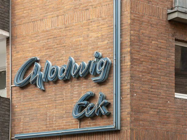 Chlodwig Eck Neonschriftzug "Chlodwig Eck" an einem Backsteingebäude, leicht verwittert, darunter das Eingangsschild.