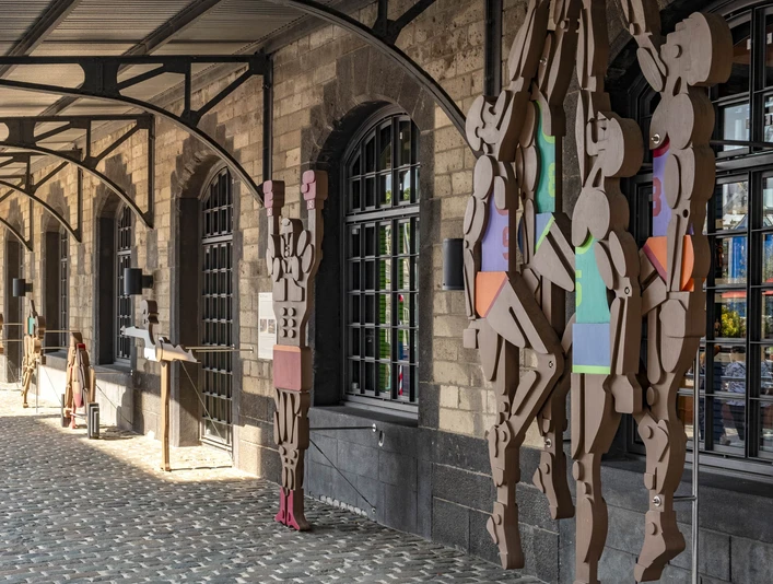 German Sport & Olympia Museum Das Bild zeigt eine überdachte Terrasse mit Figuren aus geometrischen Formen, die an Säulen lehnen.The picture shows a covered terrace with figures of geometric shapes leaning against pillars.
