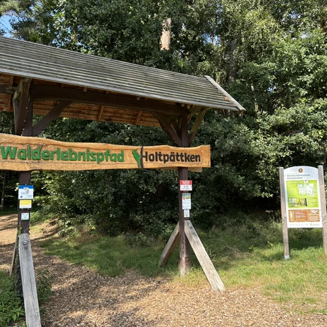 Frerener Holtpättken ©Emsland Tourismus GmbH (1).JPEG Eingang des Walderlebnispfads Holtpättken mit hölzernem Torbogen und Infotafel im grünen Wald.