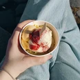 Madeleines-Homemade-Ice-Cream-Eisdiele-Bielefeld-Teutoburger-Wald-Tourismus.png Eine Hand hält einen Becher mit Vanille- und Erdbeereis, sitzend auf einer Pflastersteintreppe.