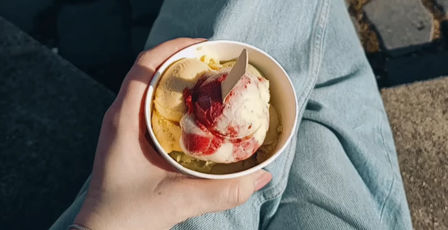 Madeleines-Homemade-Ice-Cream-Eisdiele-Bielefeld-Teutoburger-Wald-Tourismus.png Eine Hand hält einen Becher mit Vanille- und Erdbeereis, sitzend auf einer Pflastersteintreppe.
