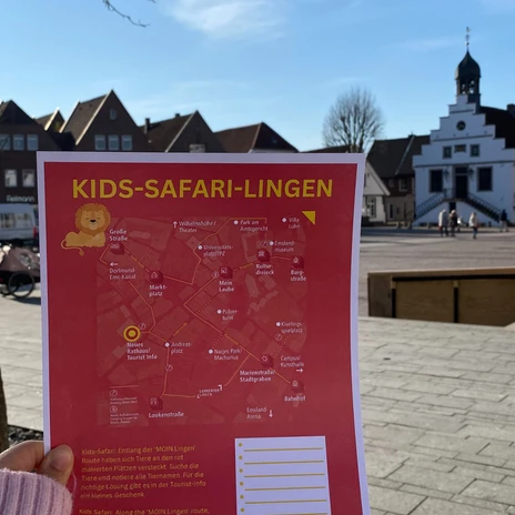 jpg (6).jpg Eine Hand hält einen Stadtplan zur Kids-Safari-Lingen vor dem sonnigen Marktplatz mit Rathaus.