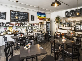 Bistro GreenBee Innenansicht Tische mit Stühlen sowie ein Regal mit Bio-Lebensmitteln im Bistro GreenBee